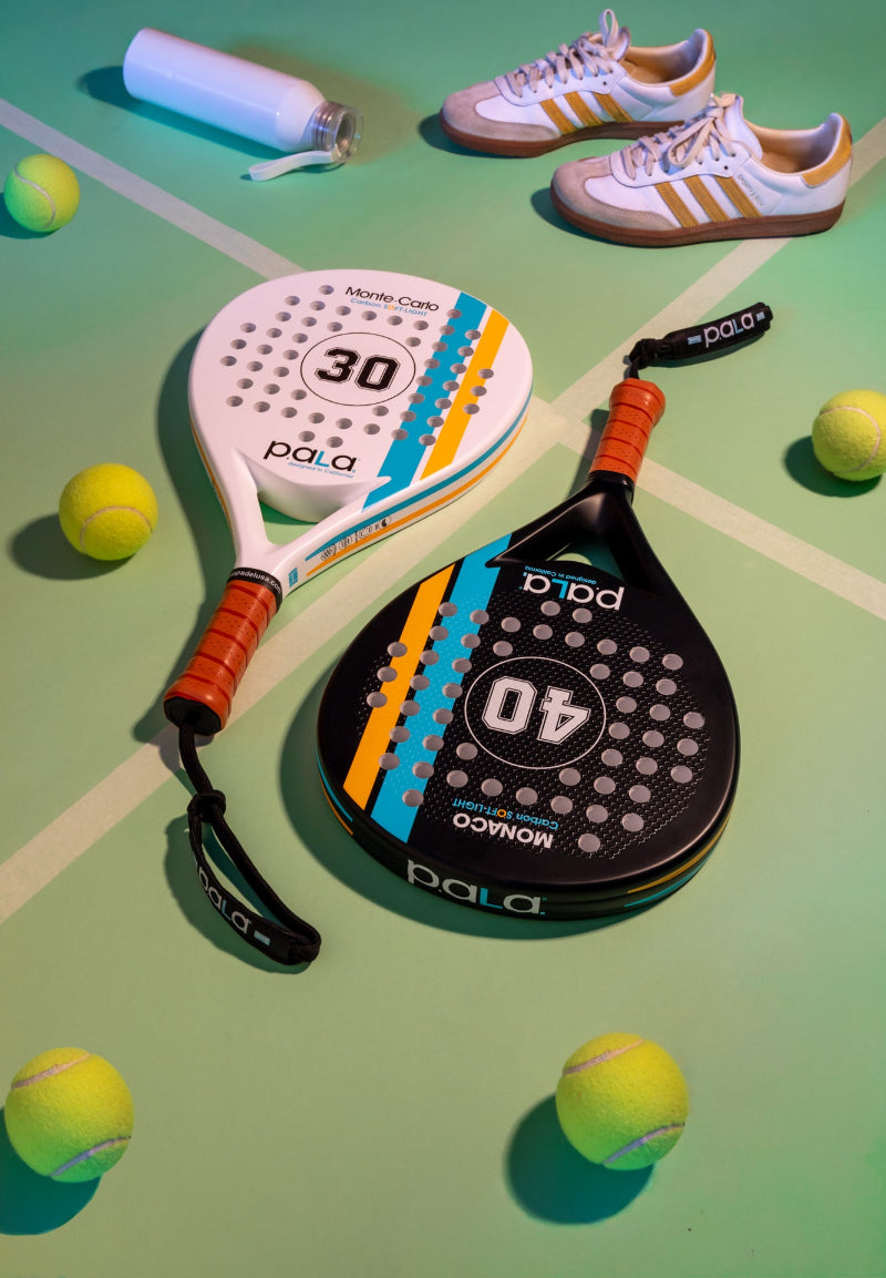 Paddle and racket with 'pala' branding on a green surface with tennis balls.