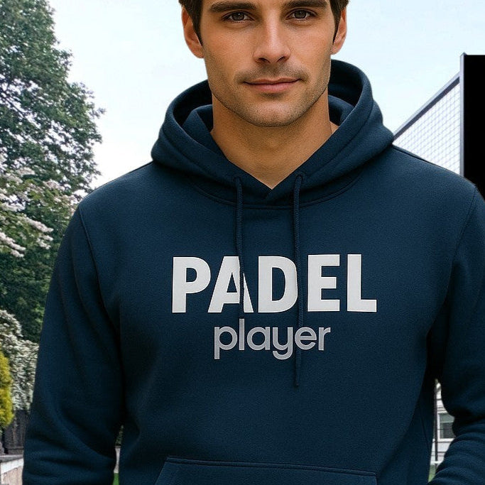 Man wearing a navy blue hoodie with the words 'PADEL player' printed on the chest in white. The sleeve features the brand name 'pala.' printed vertically. He is standing on a padel court with a net and trees in the background.