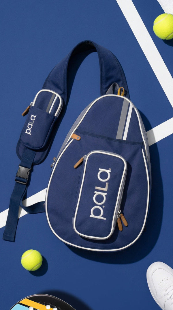 Navy blue sling bag with 'Pala' branding on a padel court background