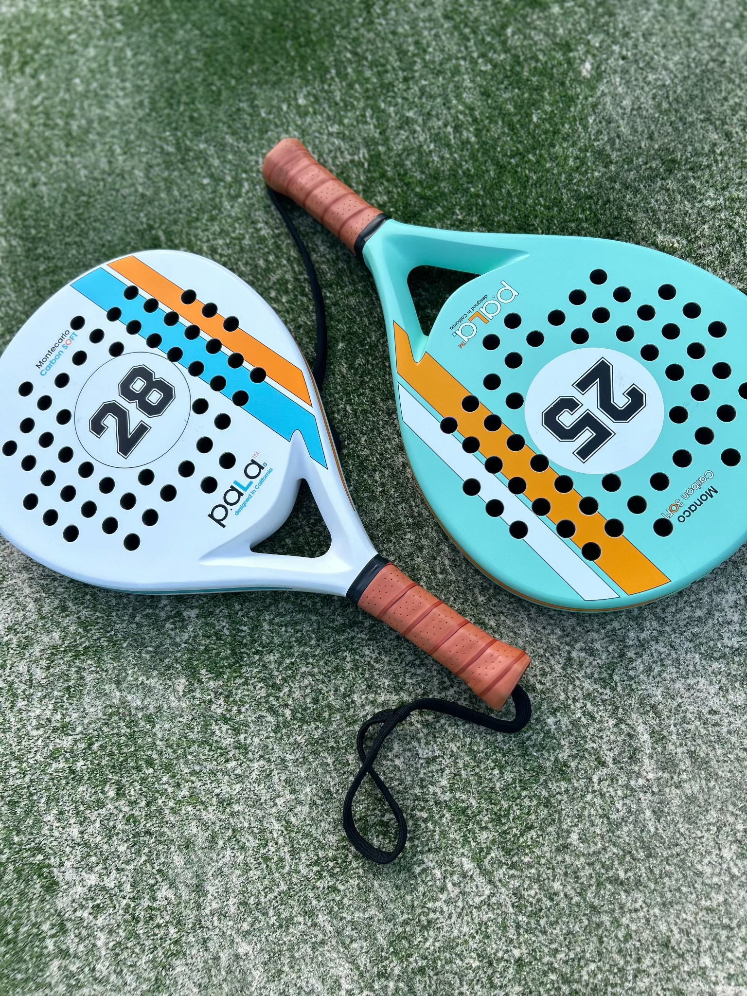 2 padel rackets on a padel court with number 25 and 28 over green grass